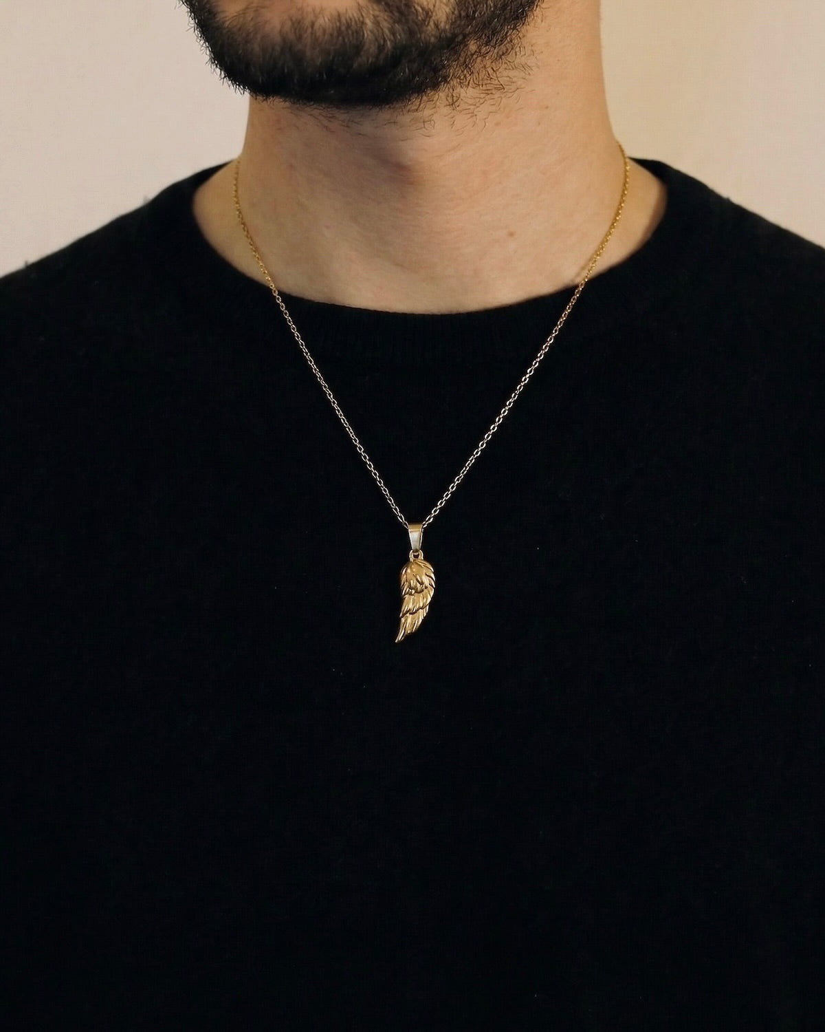 Man wearing a gold angel wing necklace on a 50cm chain over a black t-shirt