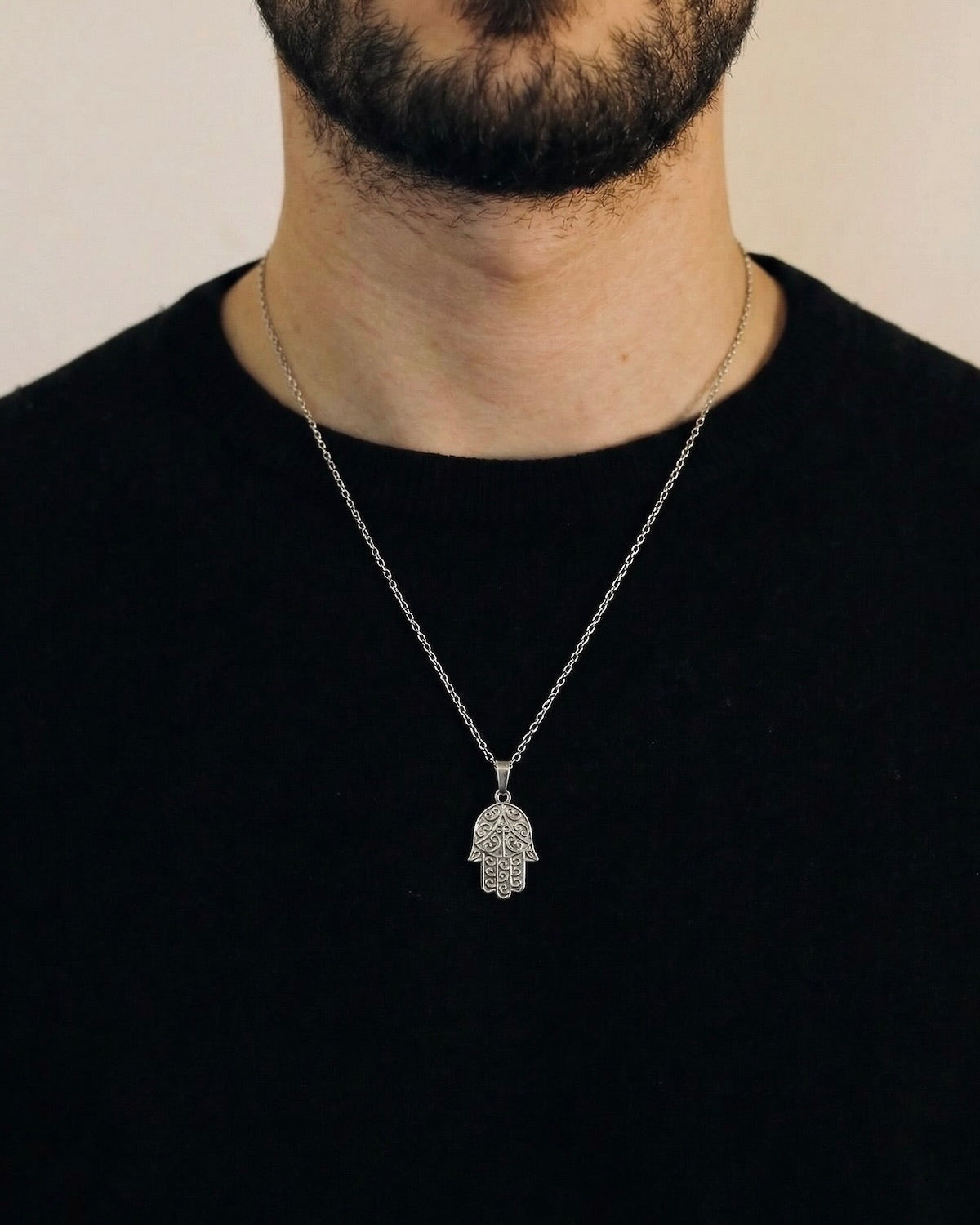 Man wearing a silver hamsa hand necklace on a 50cm chain over a black t-shirt