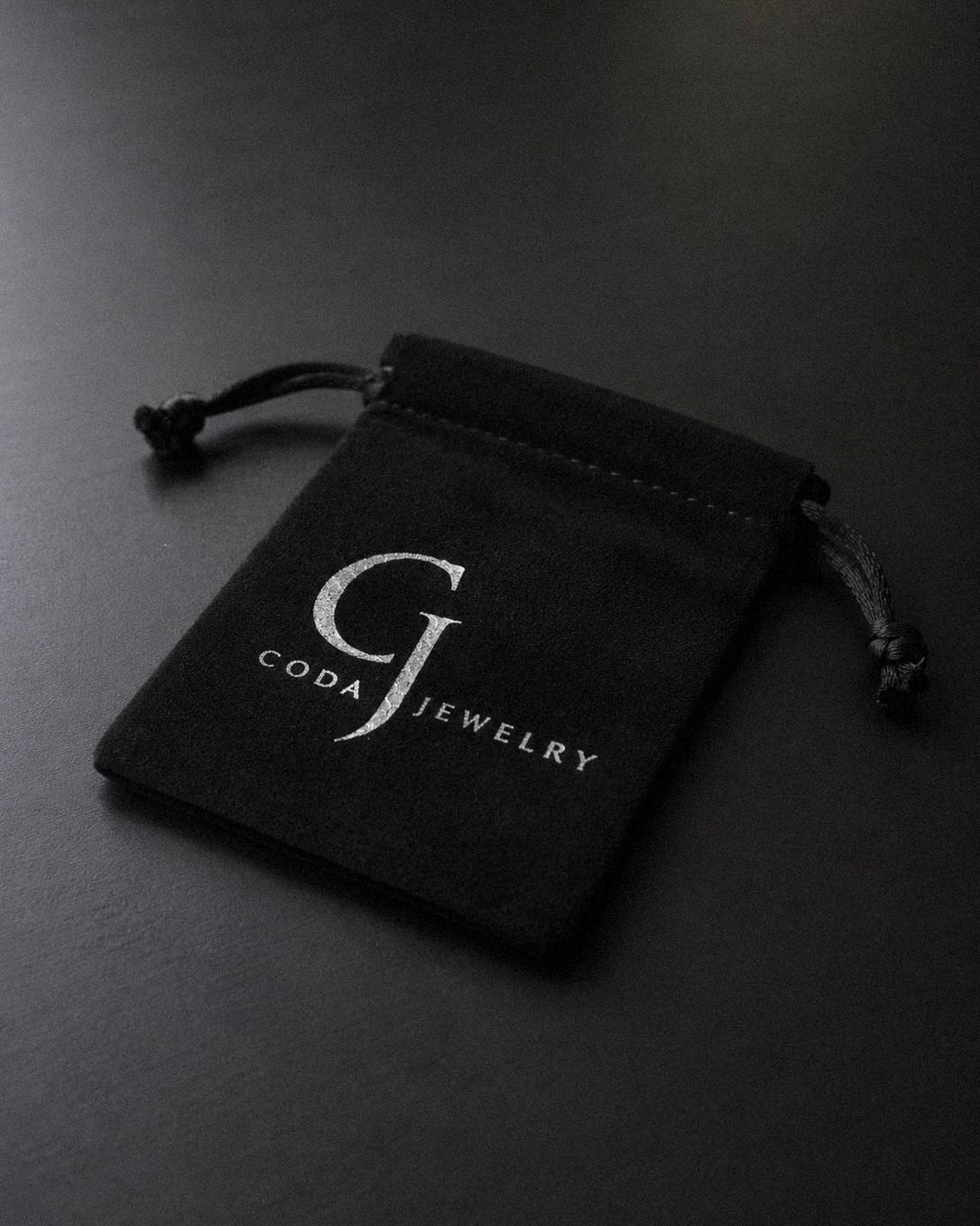 A small black velvet jewelry pouch with a drawstring closure, featuring the 'GODA JEWELRY' logo printed in white on the front, set against a dark gray background.