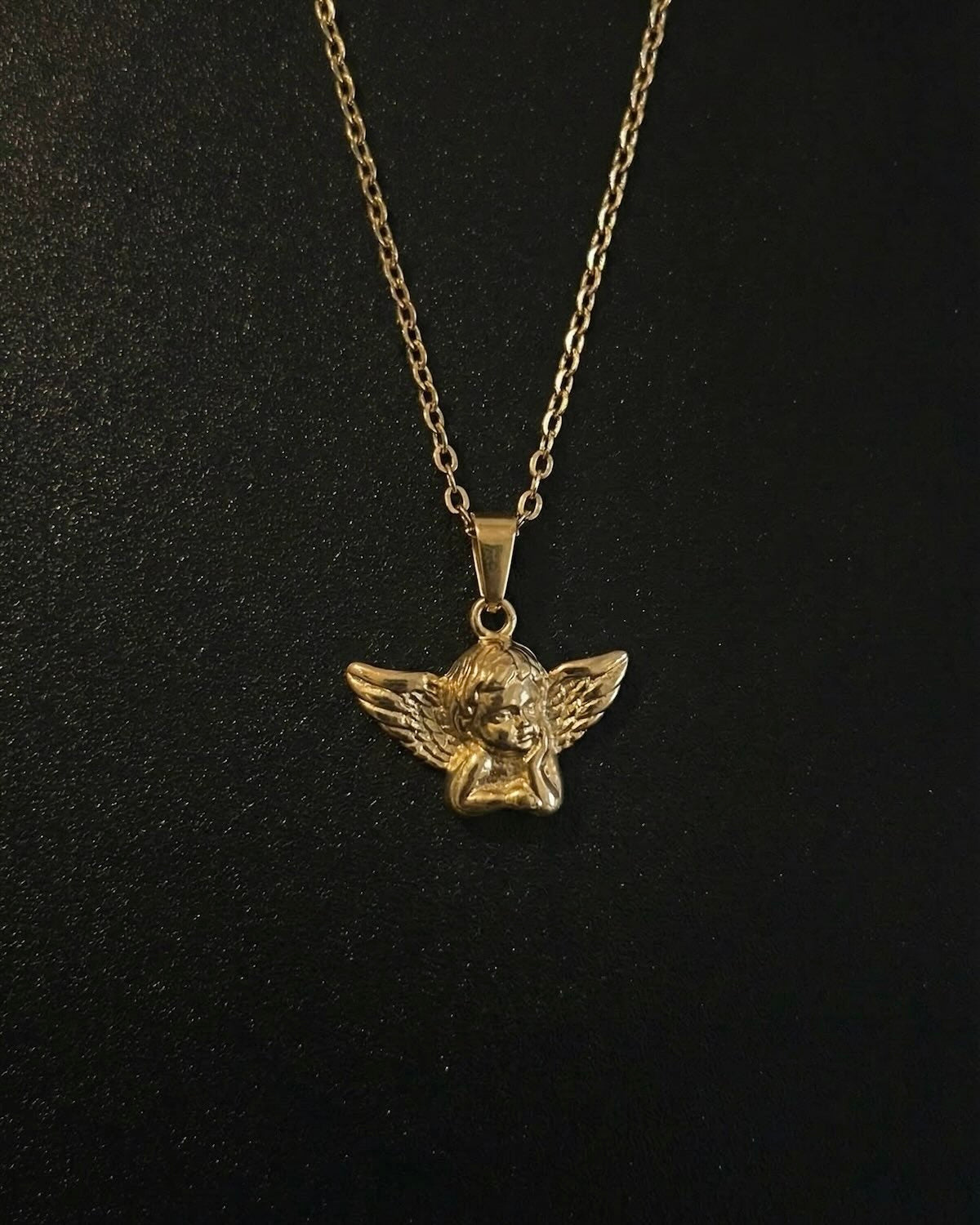 Gold angel pendant shaped into a 3D cherub with spread feathered wings, close detail