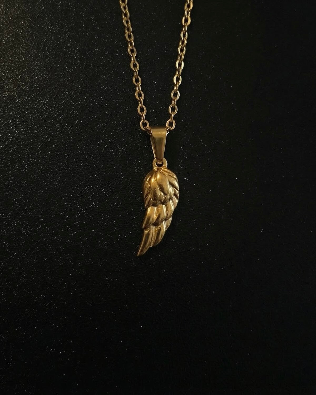 Gold angel wing pendant with layered feathers and a polished finish, close detail