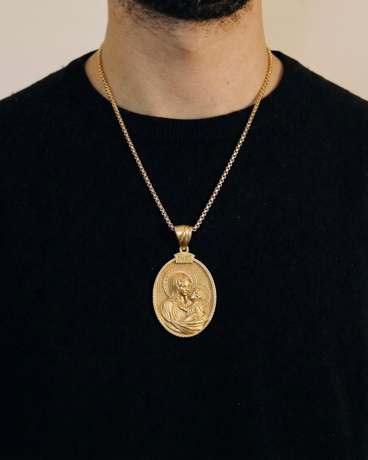 Man wearing a gold baby Jesus necklace on a 50cm chain over a black t-shirt