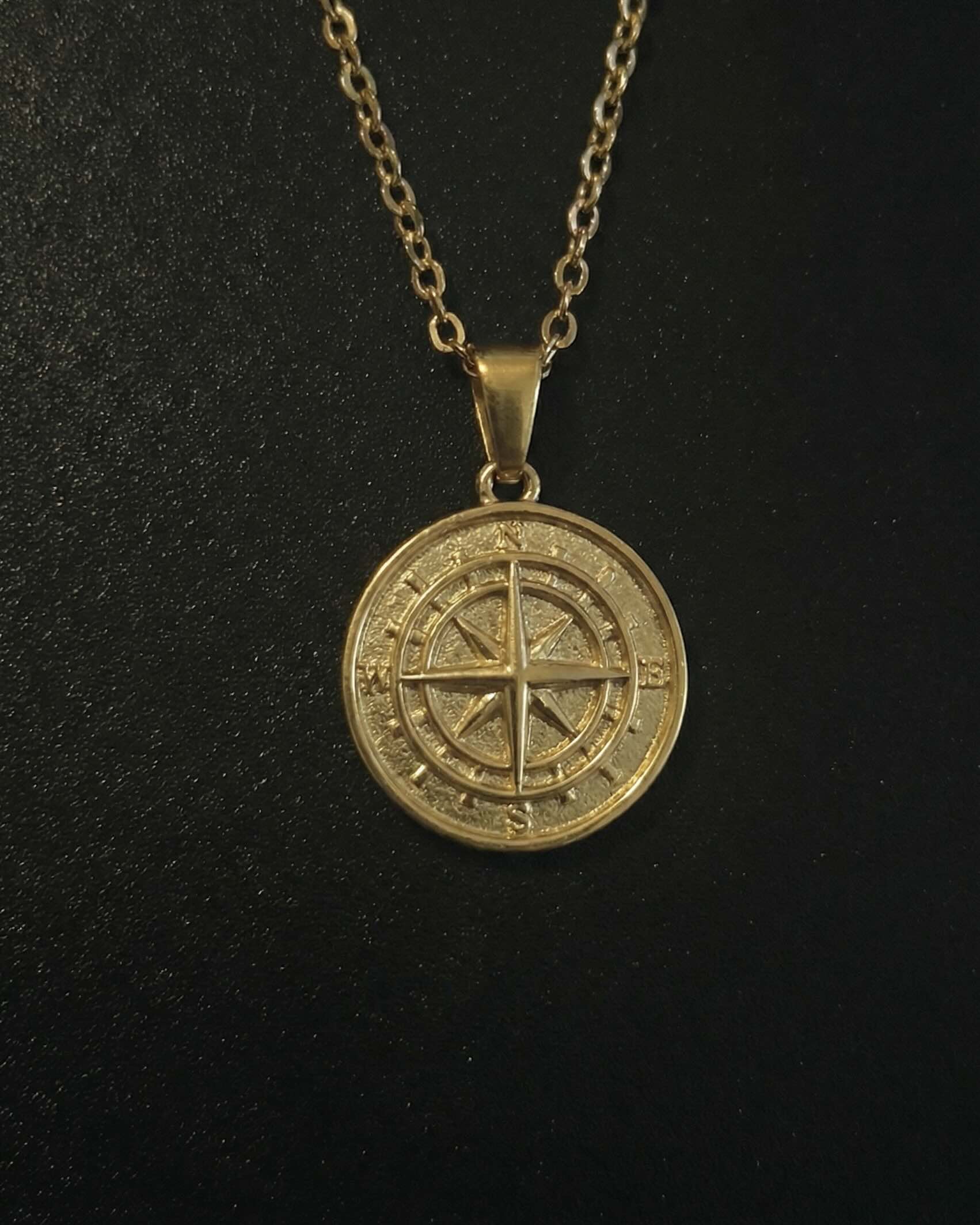 Gold compass pendant with a compass rose and four-point star on a solid medallion, close detail