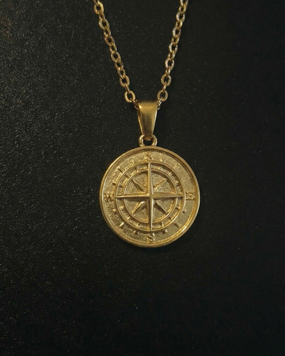 Gold compass pendant with a compass rose and four-point star on a solid medallion, close detail