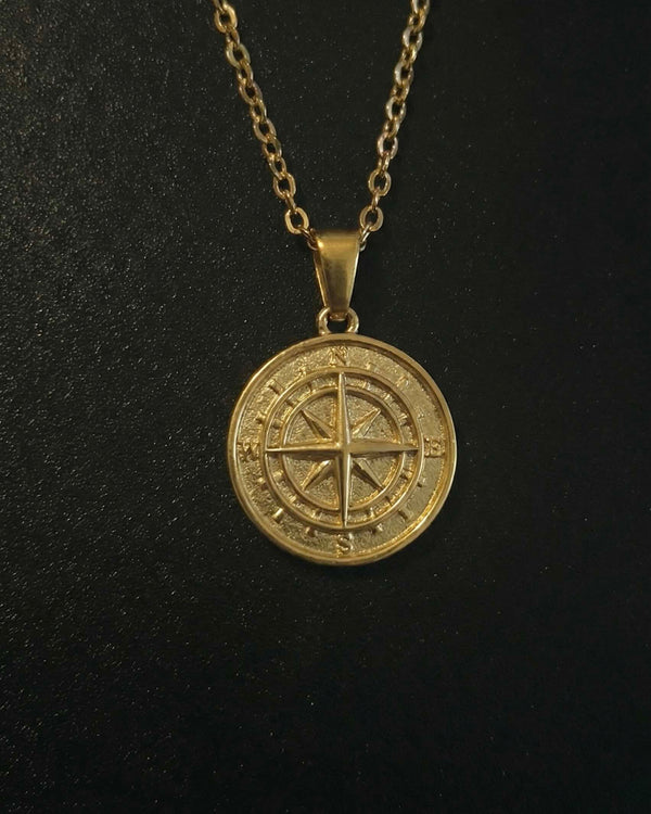 Gold compass pendant with a compass rose and four-point star on a solid medallion, close detail