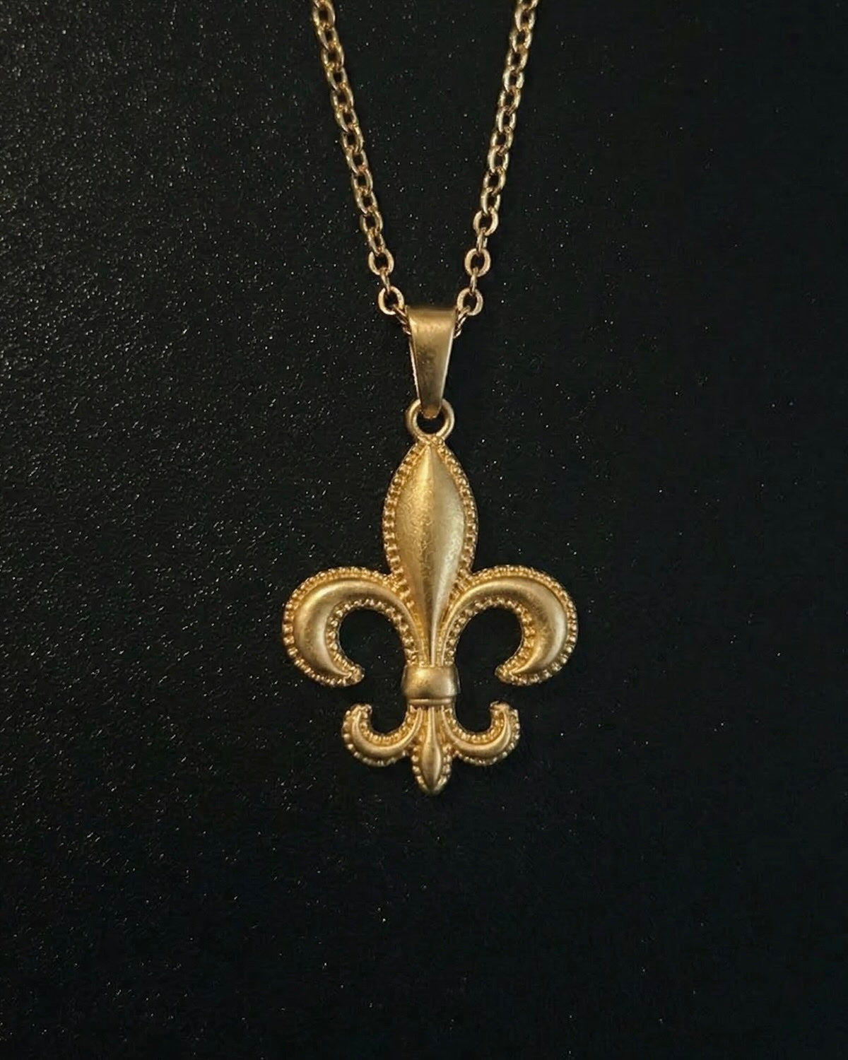 Gold fleur-de-lis pendant with a beaded milgrain edge and brushed finish, close detail