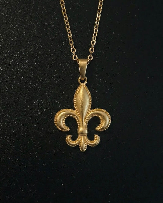 Gold fleur-de-lis pendant with a beaded milgrain edge and brushed finish, close detail