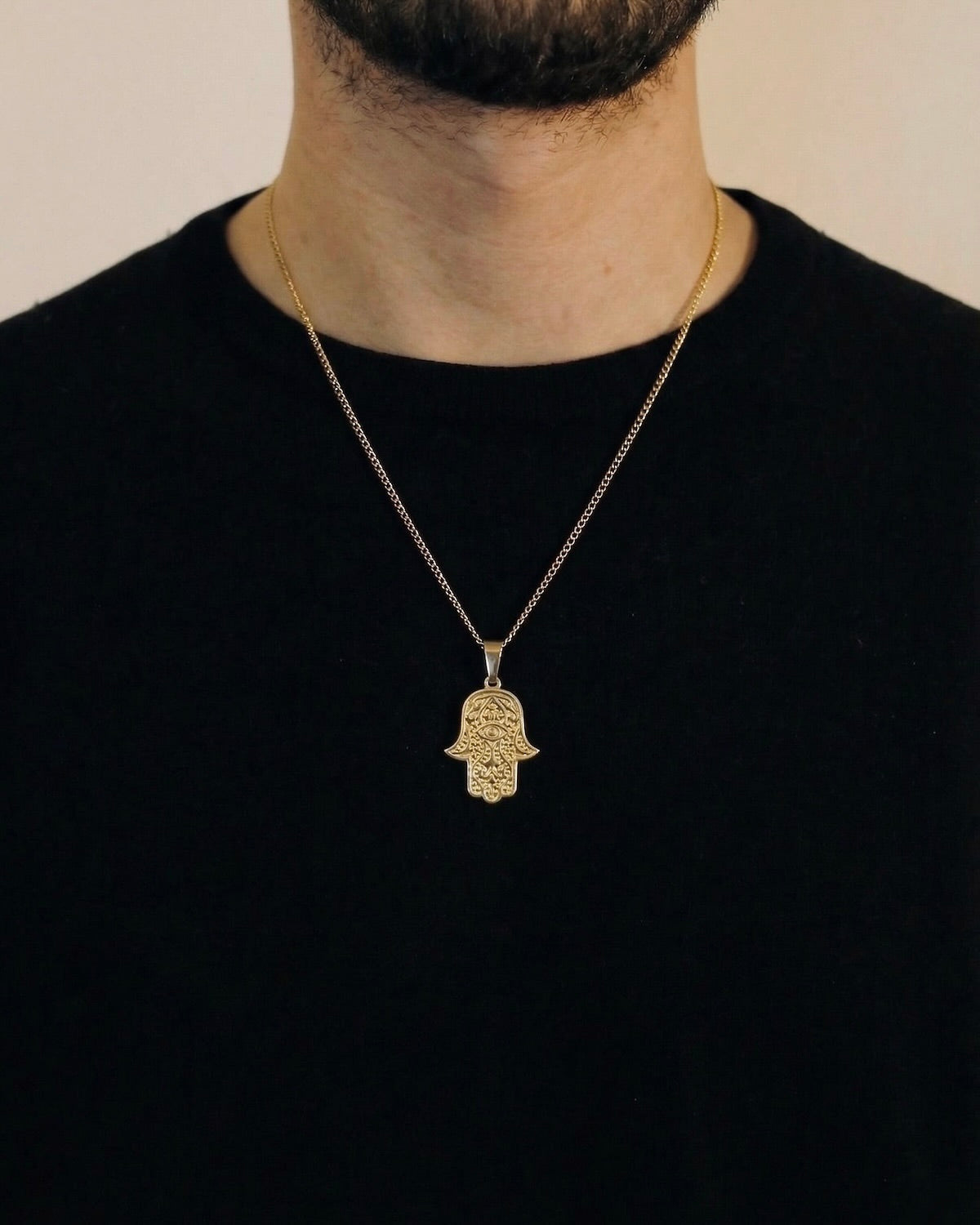 Man wearing a gold hamsa evil eye necklace on a 50cm chain over a black t-shirt