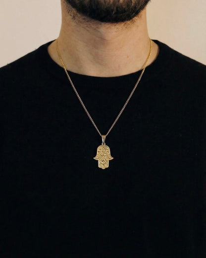 Man wearing a gold hamsa evil eye necklace on a 50cm chain over a black t-shirt