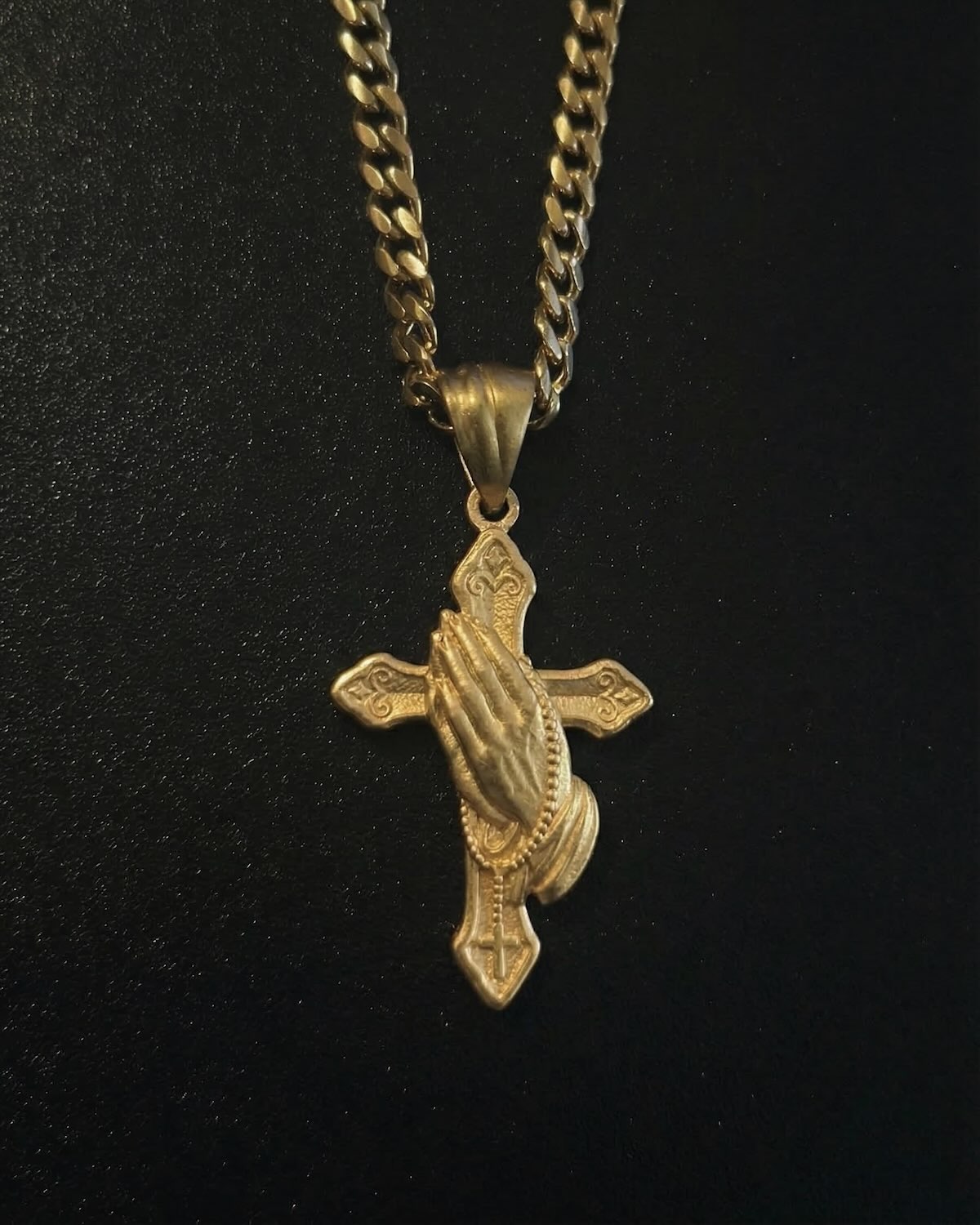 Gold hand cross pendant with sculpted praying hands over an ornate cross, close detail