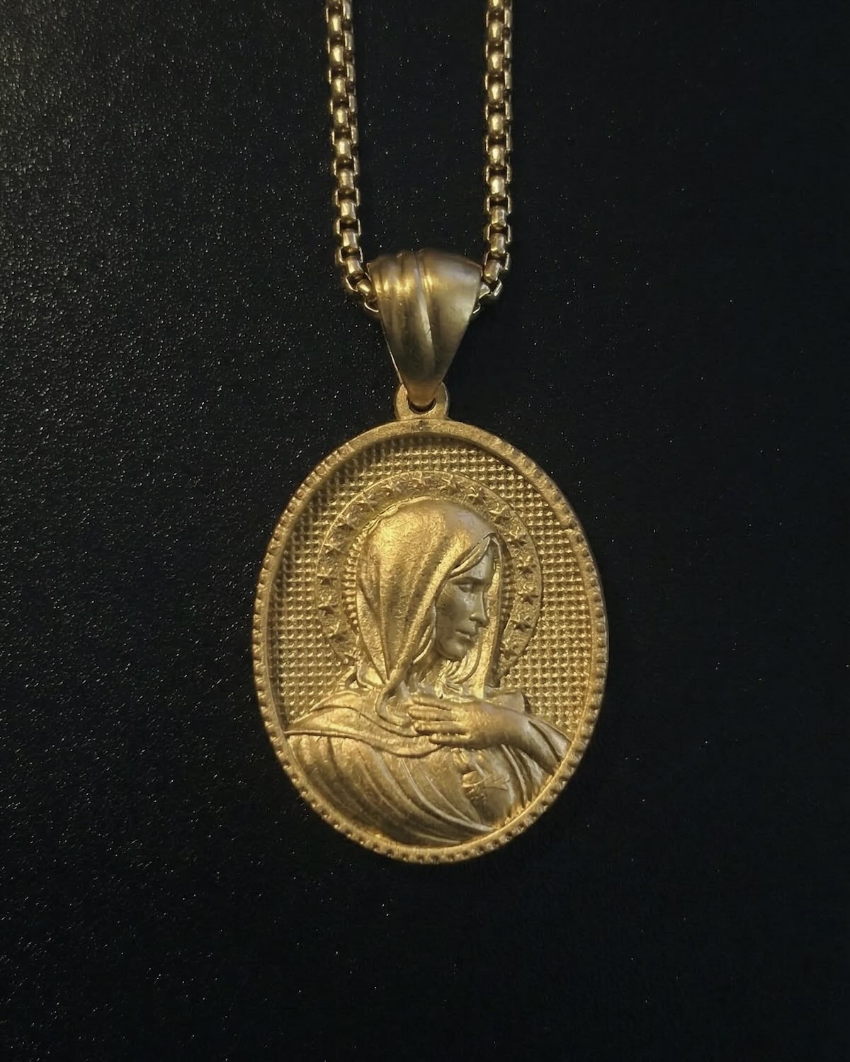 Gold Holy Mary pendant with Mary in side profile and a hand on her chest, ringed by stars, close detail