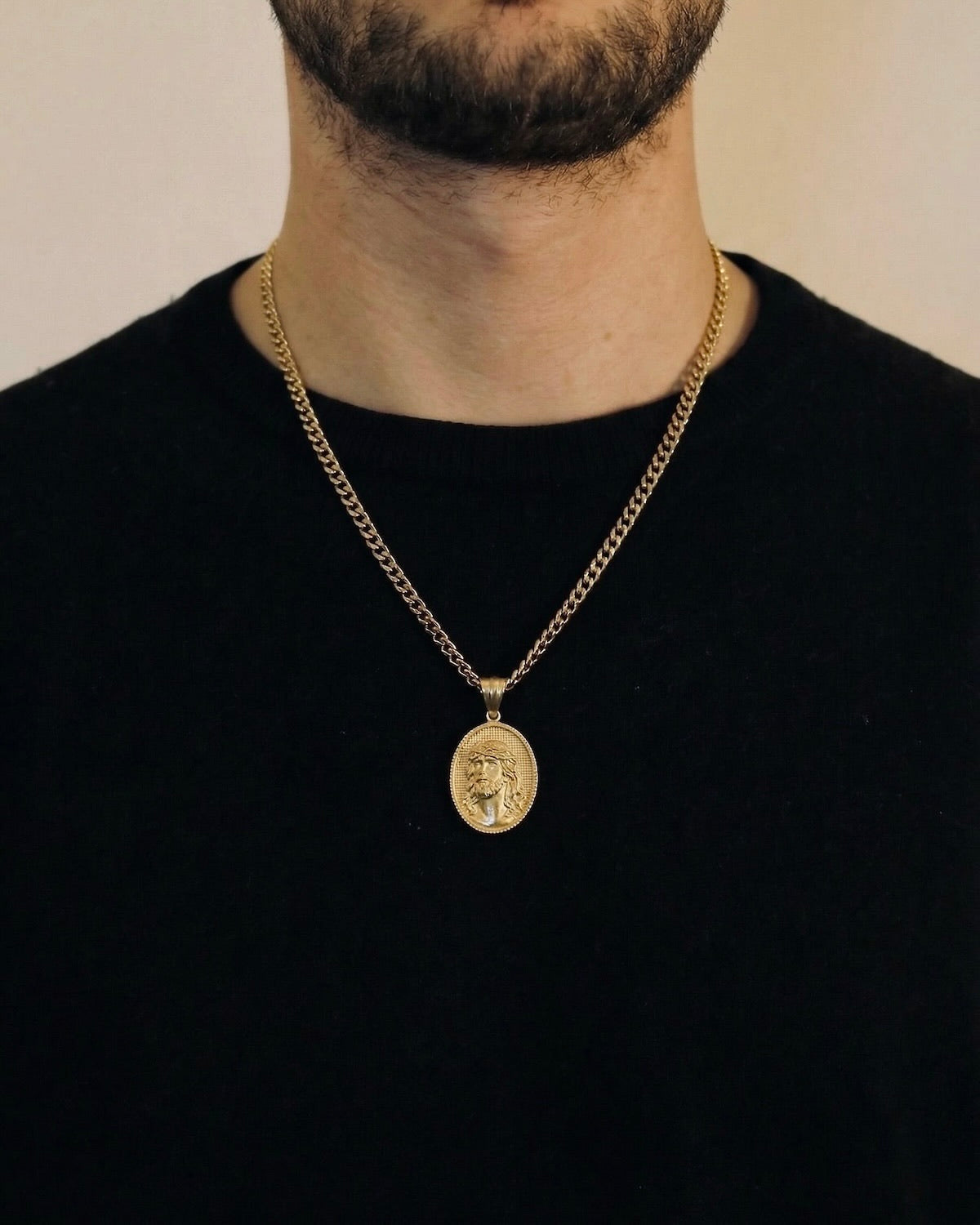 Man wearing a gold Jesus coin necklace on a 50cm chain over a black t-shirt