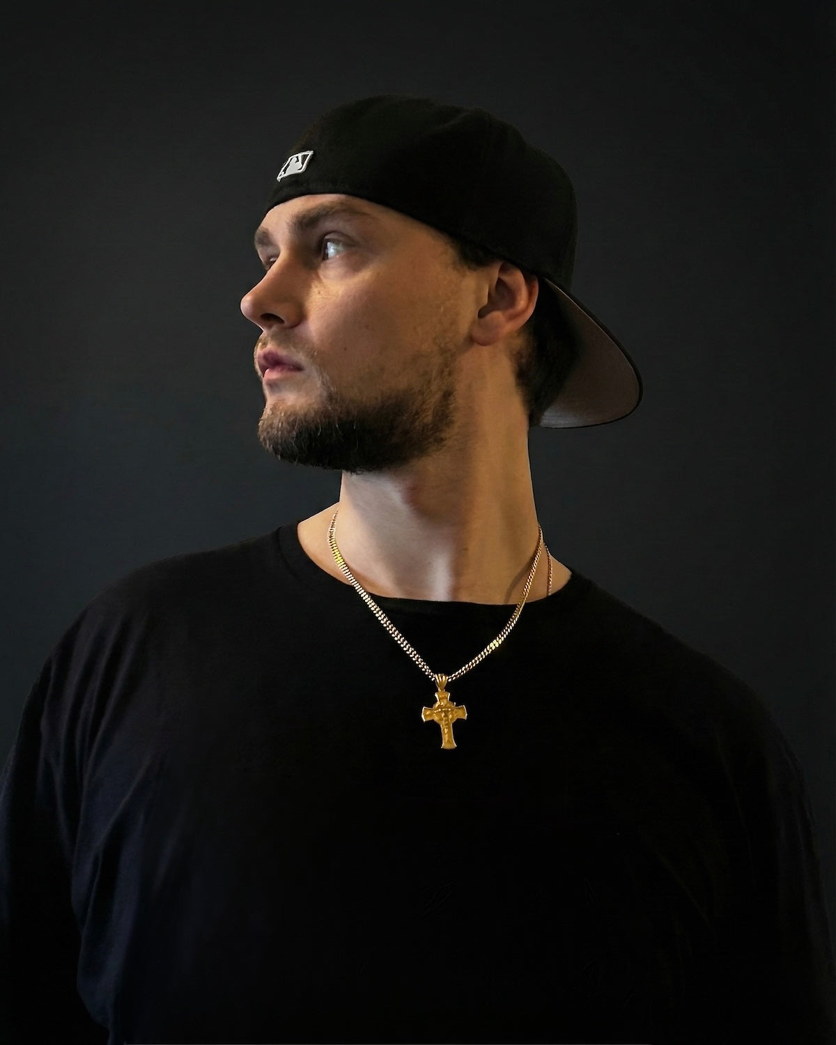 Man in a black cap and black t-shirt wearing a gold Jesus face cross necklace on a 50cm chain
