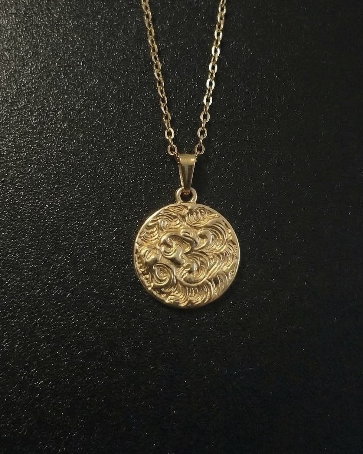Gold lion coin pendant with a lion head and flowing mane in relief, close detail
