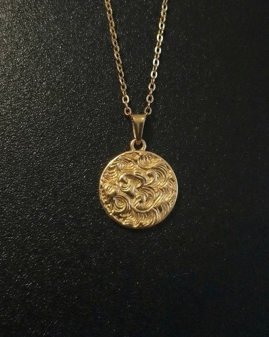 Gold lion coin pendant with a lion head and flowing mane in relief, close detail