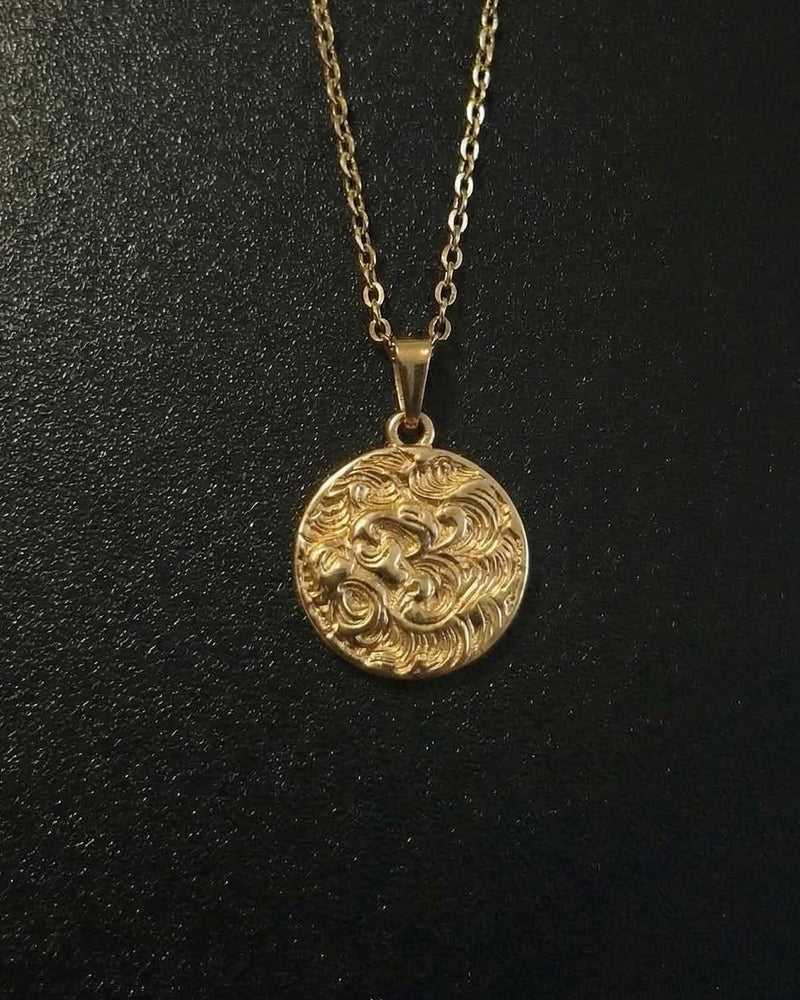 Gold lion coin pendant with a lion head and flowing mane in relief, close detail