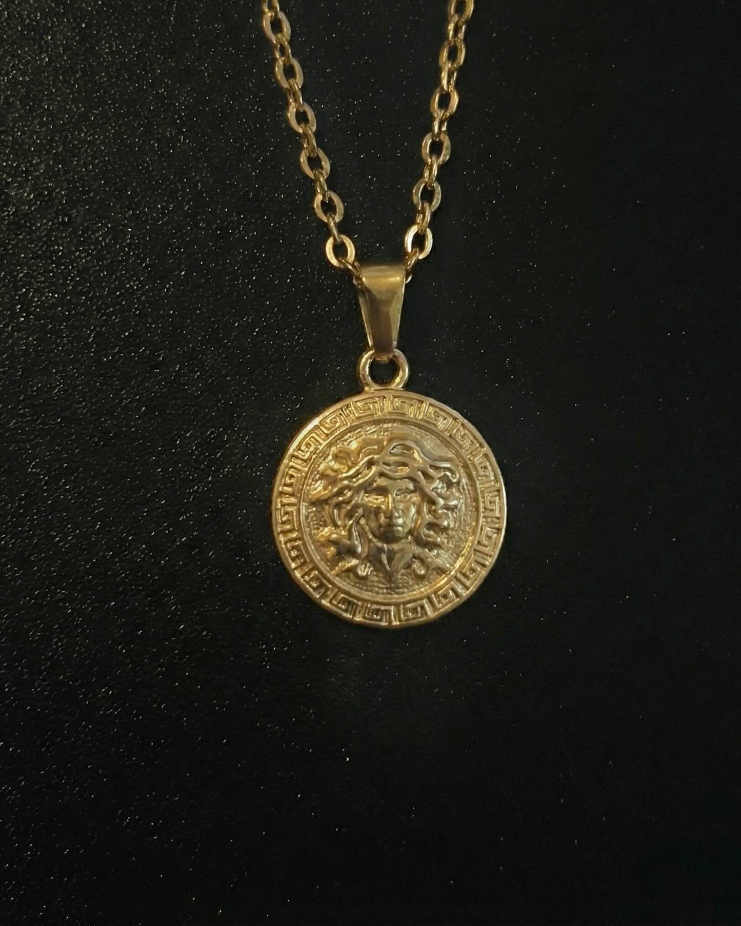 Gold medusa pendant with the Medusa head and a Greek key border, close detail