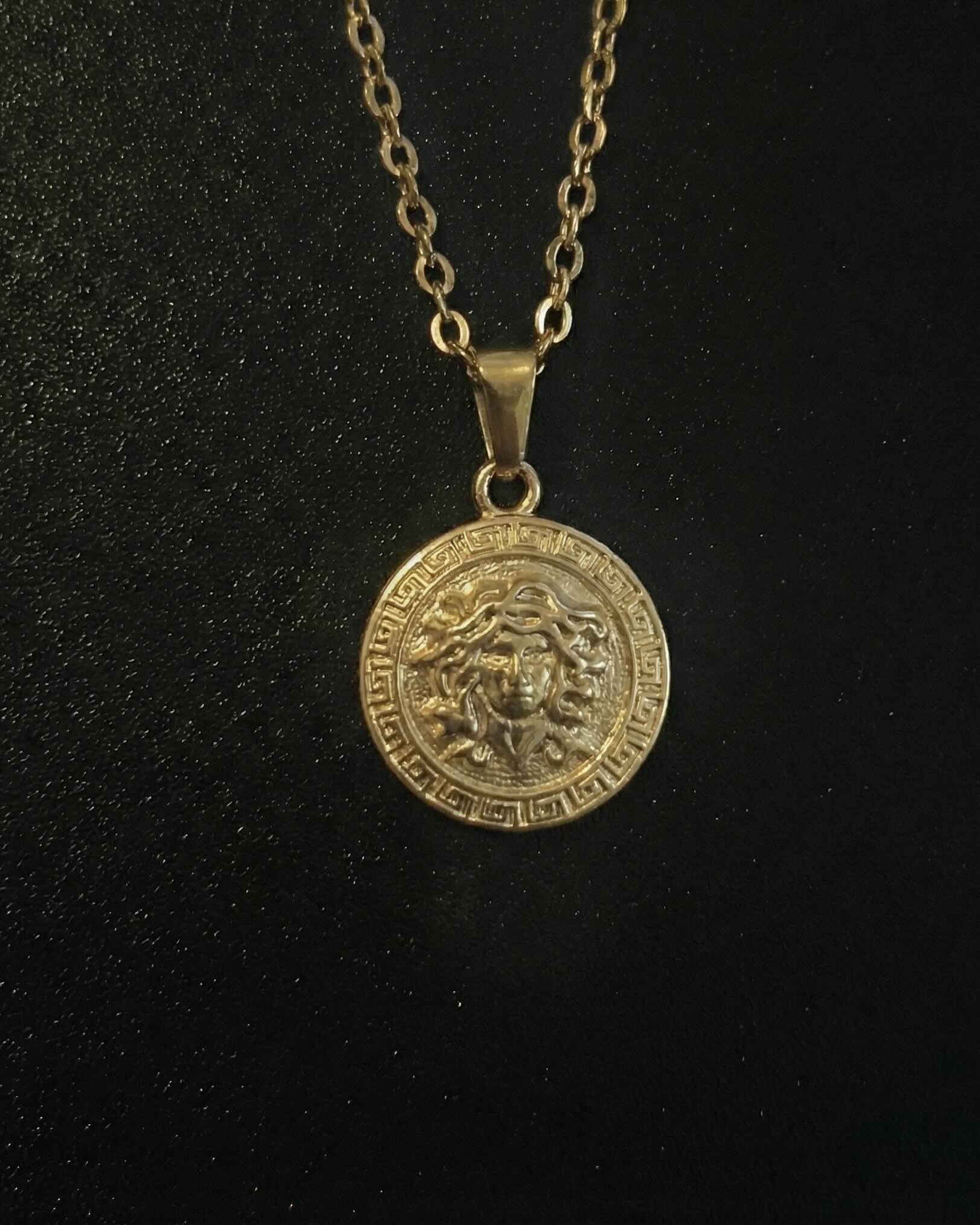 Gold medusa pendant with the Medusa head and a Greek key border, close detail