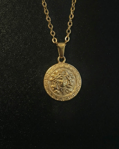 Gold medusa pendant with the Medusa head and a Greek key border, close detail