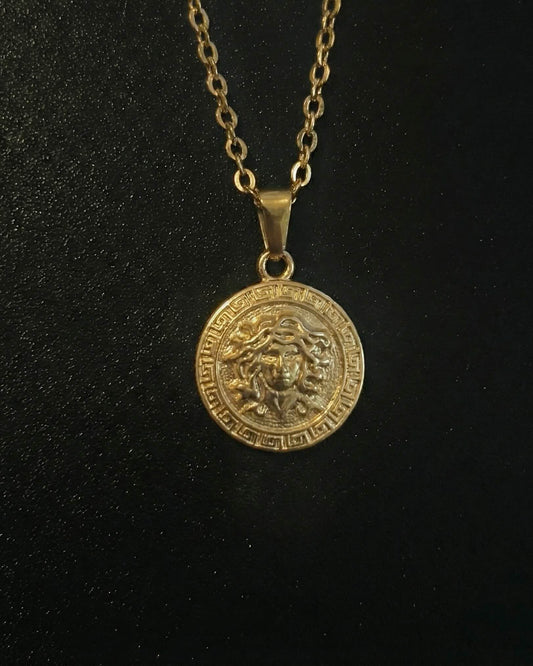 Gold medusa pendant with the Medusa head and a Greek key border, close detail