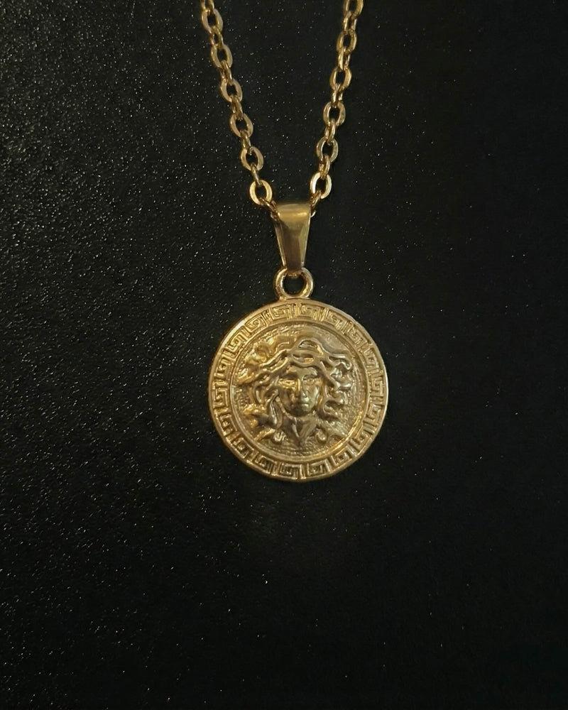 Gold medusa pendant with the Medusa head and a Greek key border, close detail