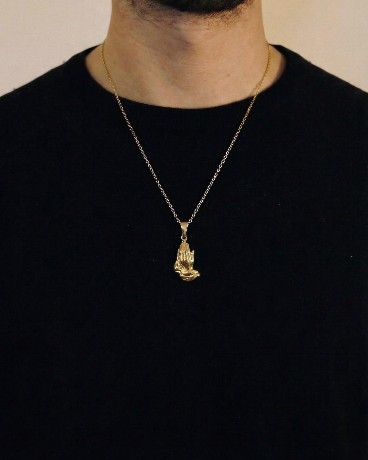 Man wearing a gold praying hands necklace on a 50cm chain over a black t-shirt