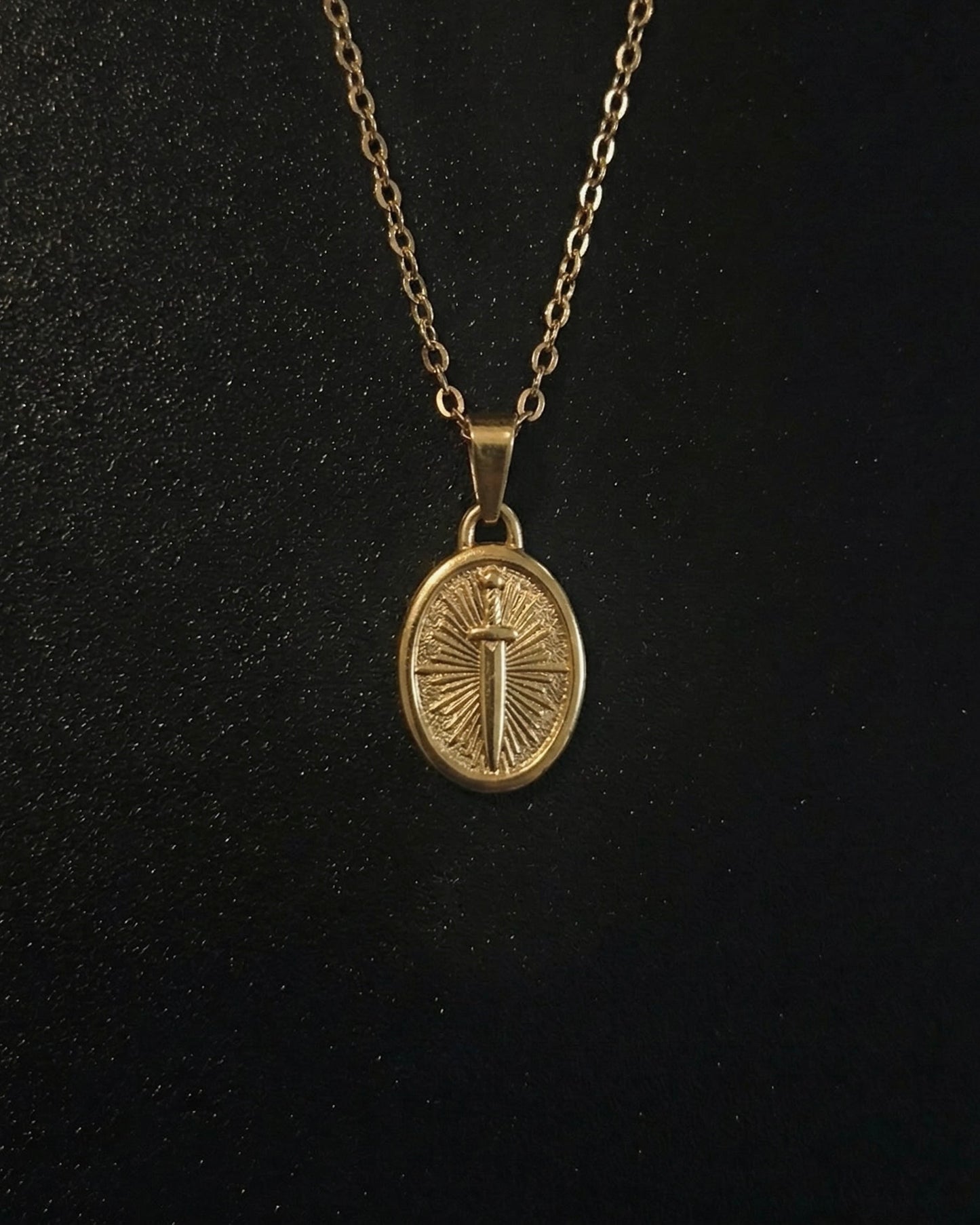 Gold sword coin pendant on an oval medallion with a dagger and sunburst, close detail