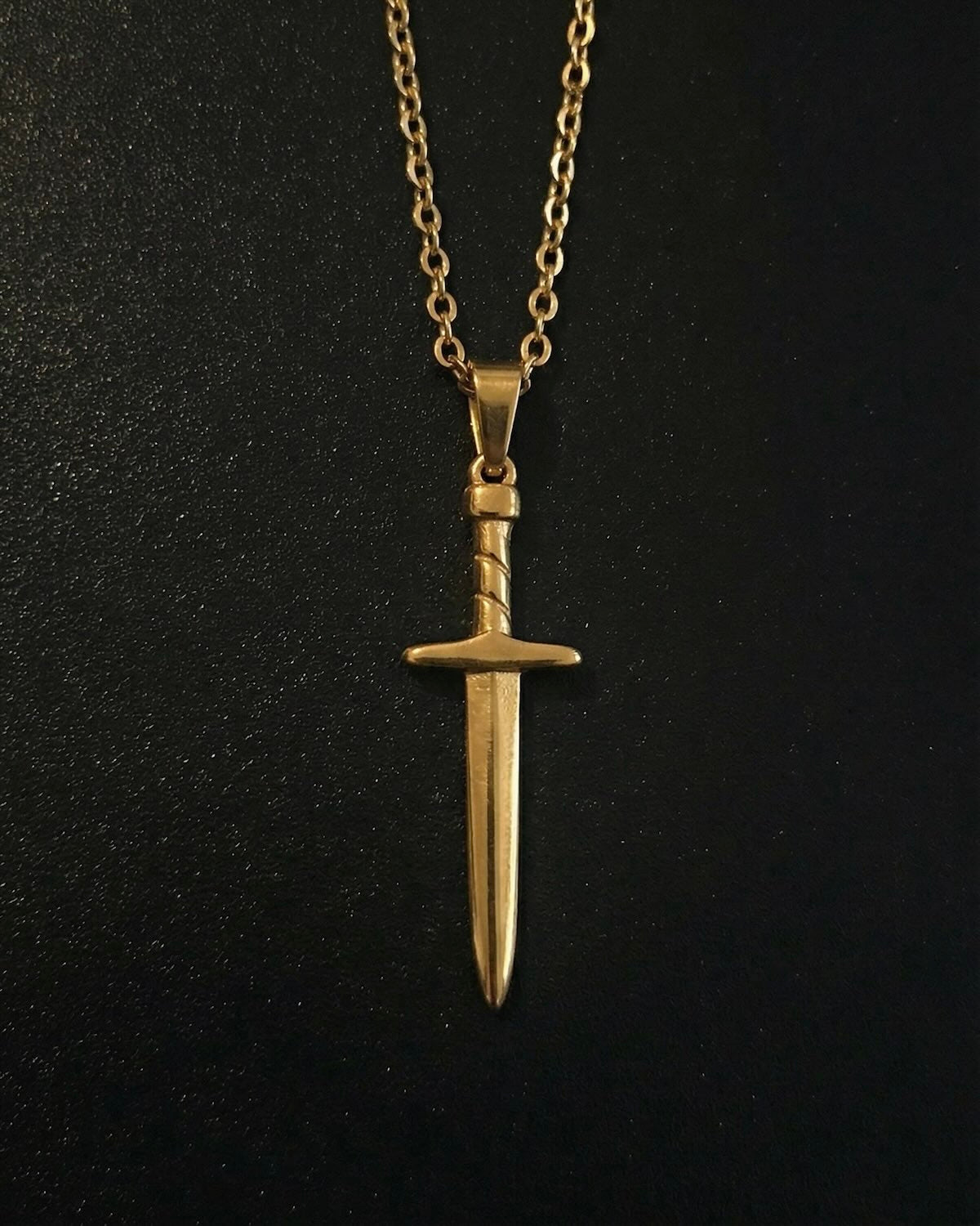 Gold sword pendant shaped like a dagger with a twisted wrapped handle, close detail