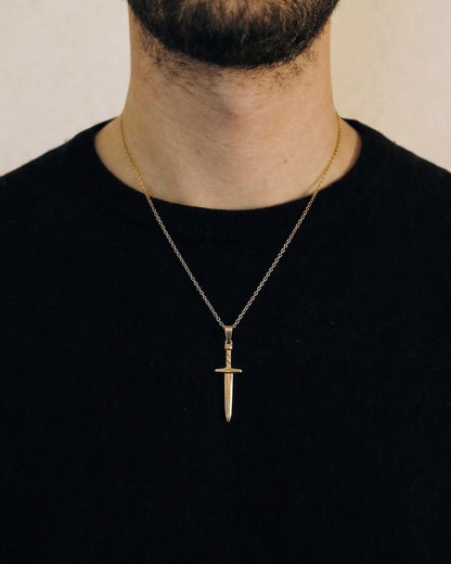 Man wearing a gold sword necklace on a 50cm chain over a black t-shirt