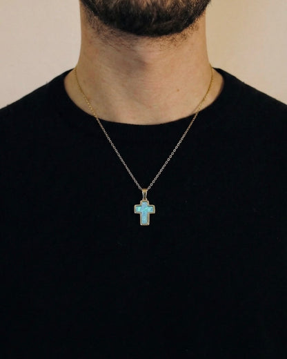 Man wearing a gold trimmed cross necklace with a blue opal center on a 50cm chain over a black t-shirt