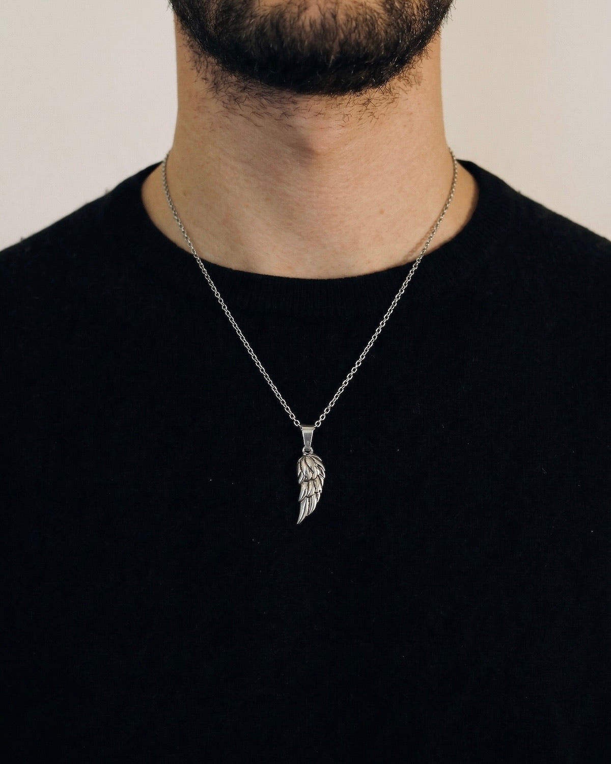 Man wearing a silver angel wing necklace on a 50cm chain over a black t-shirt