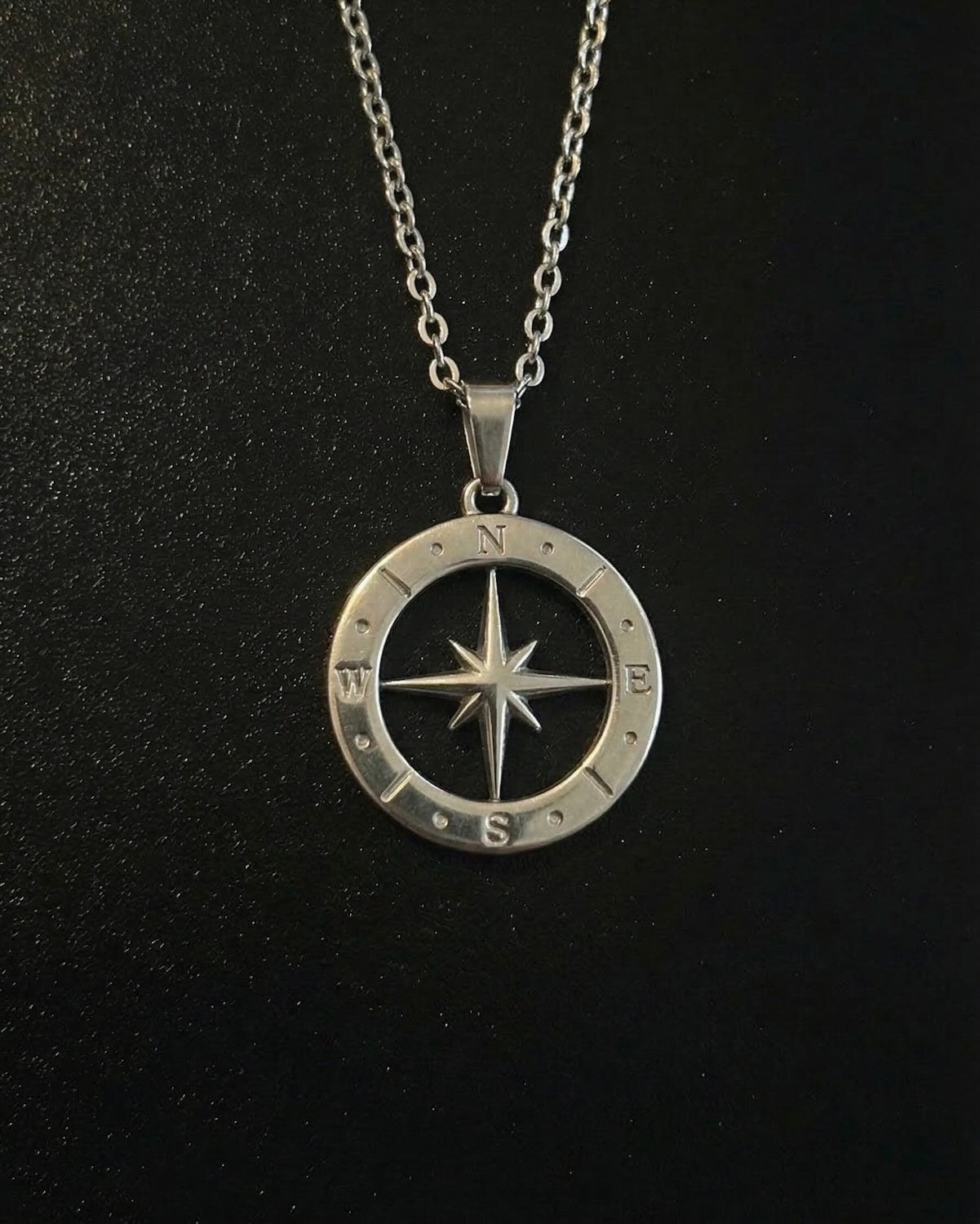 Silver open compass pendant with a cut-out star inside a ring of compass markings, close detail