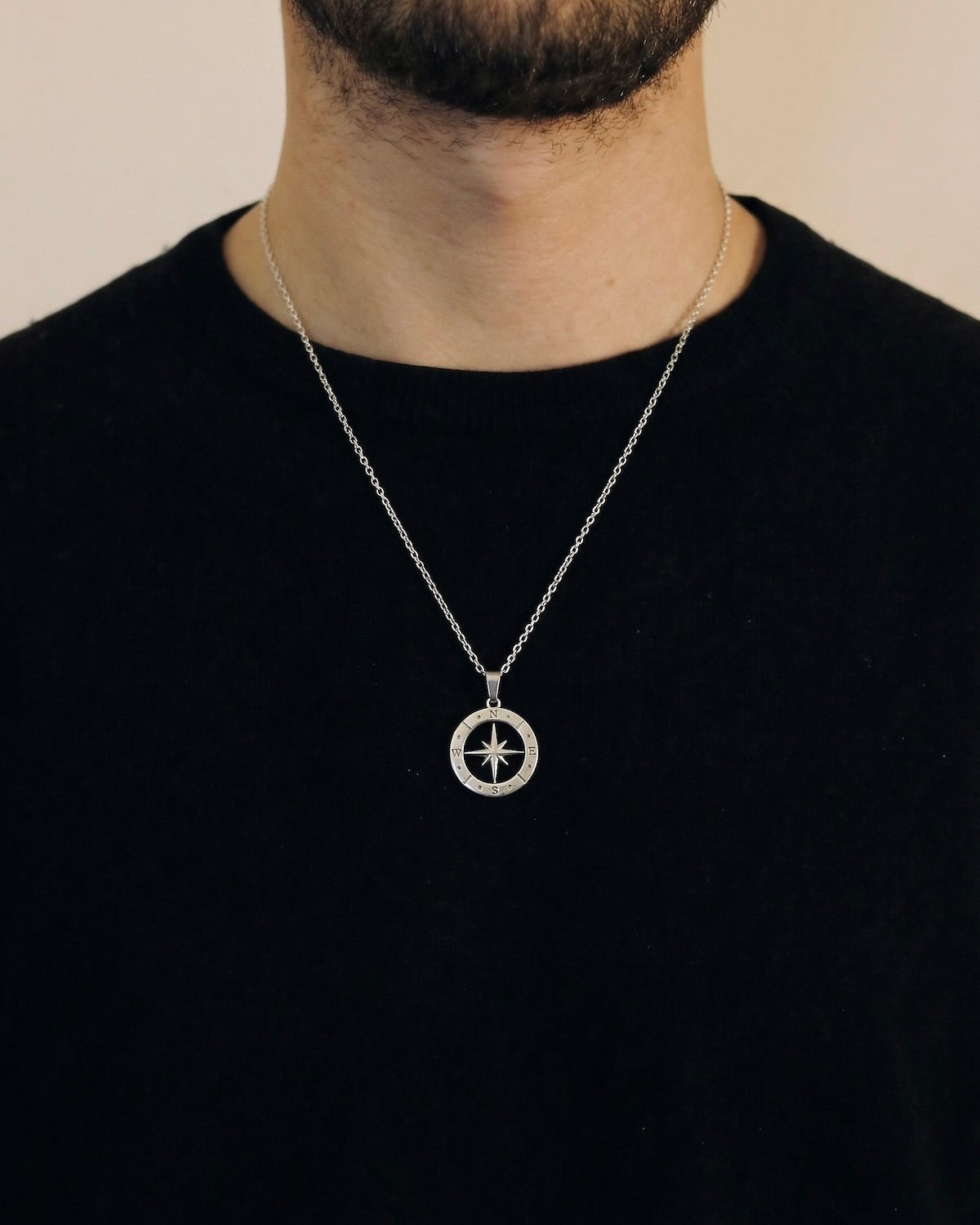 Man wearing a silver open compass necklace on a 50cm chain over a black t-shirt