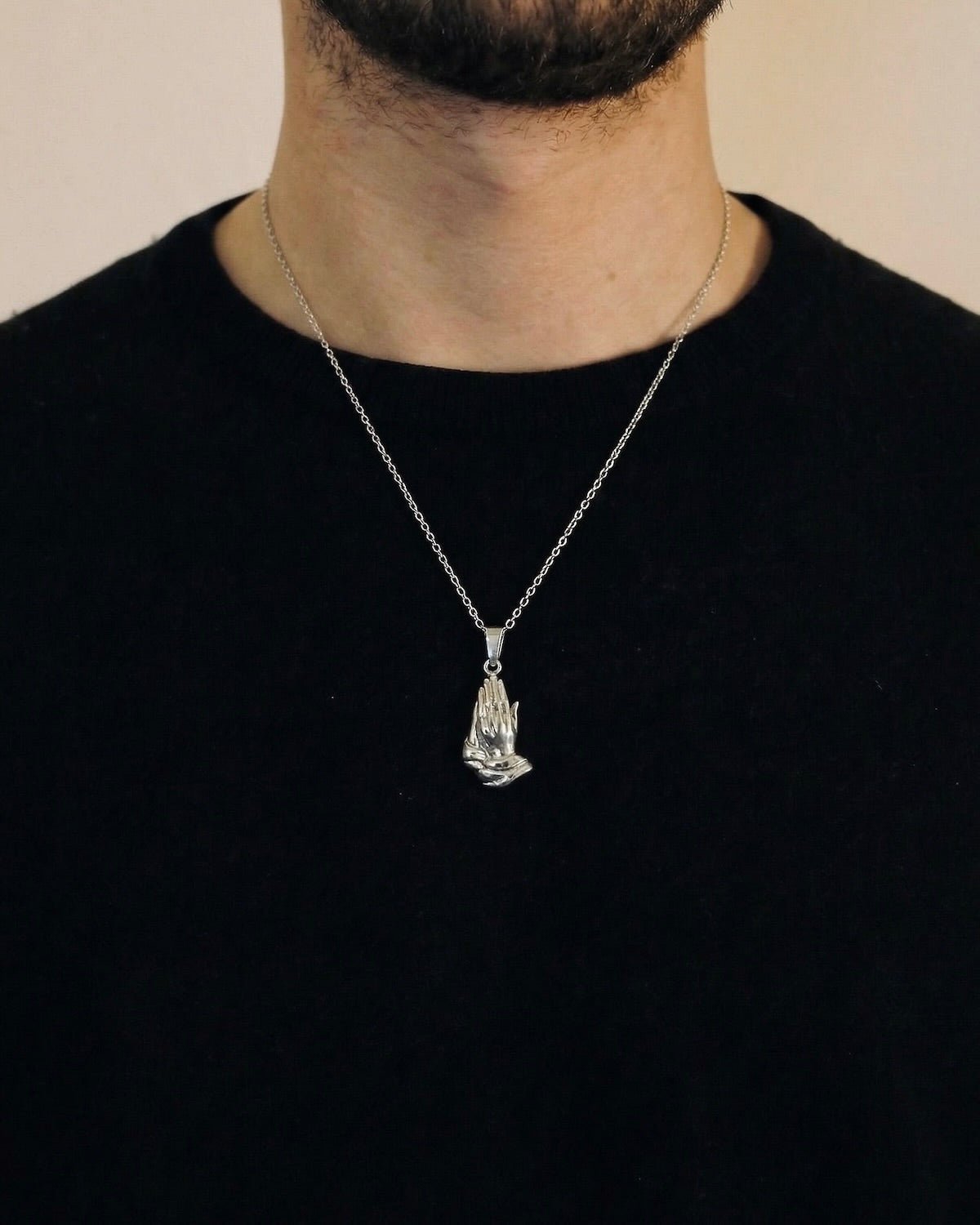 Man wearing a silver praying hands necklace on a 50cm chain over a black t-shirt