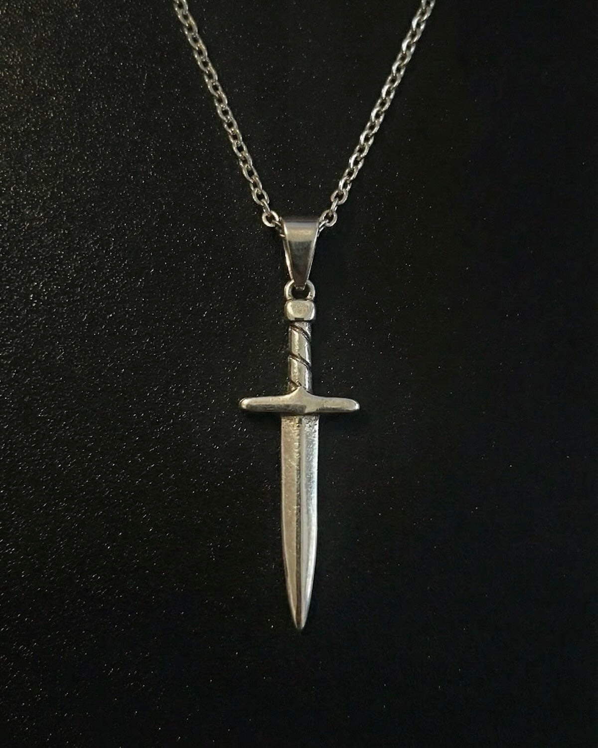 Silver sword pendant shaped like a dagger with a twisted wrapped handle, close detail