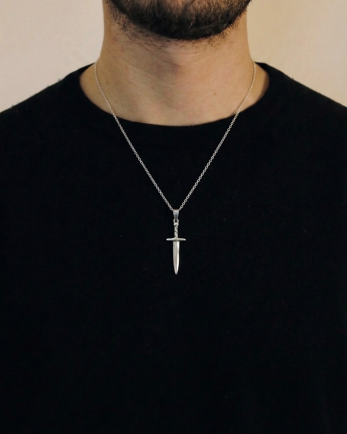 Man wearing a silver sword necklace on a 50cm chain over a black t-shirt